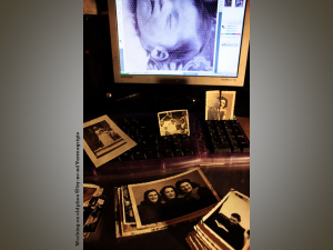 Family snapshots laid out across a computer keyboard, with a scanned image from another snapshot visible on the computer monitor