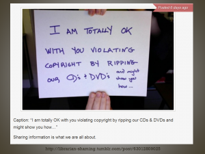 Photo of two hands holding up a andwritten sign that says "I am totally okay with you violating copyright by ripping our CDs & DVDs... and might show you how"