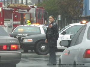 Photo of a policewoman directing traffic in the rain, with police cars and a fire truck behind her