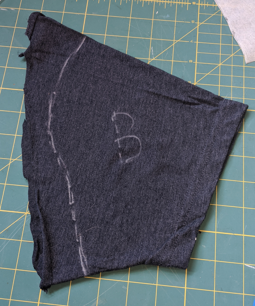 Cut-off-t-shirt sleeve lying on a green cutting mat. It has a sleeve pattern piece traced onto it in chalk, and is labeled "B" for Back.