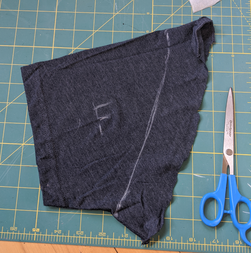 Cut-off-t-shirt sleeve lying on a green cutting mat. It has a sleeve pattern piece traced onto it in chalk, and is labeled "F" for front.